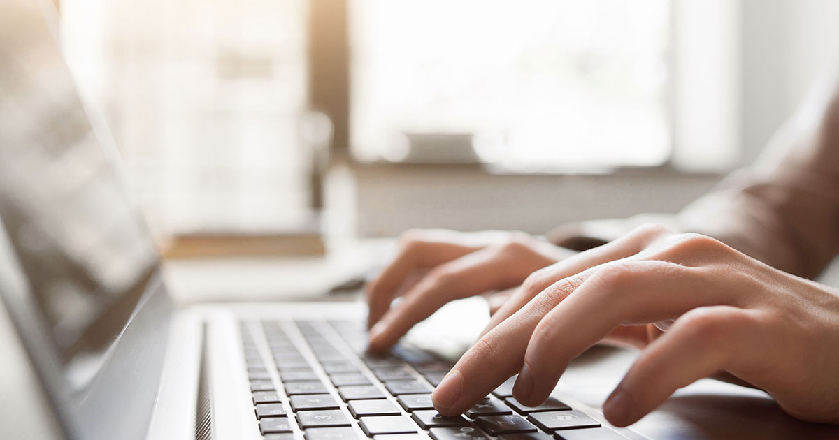 Closeup of hands typing on a laptop keyboard.