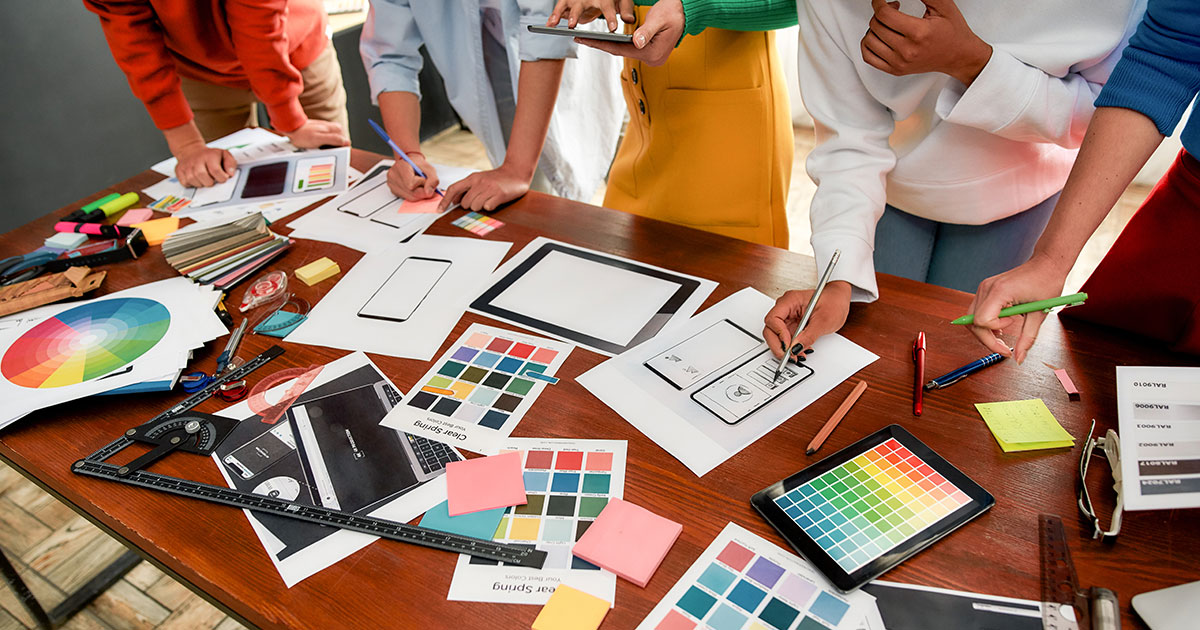 A design team is going over color schemes and typography with papers and samples on the desk.