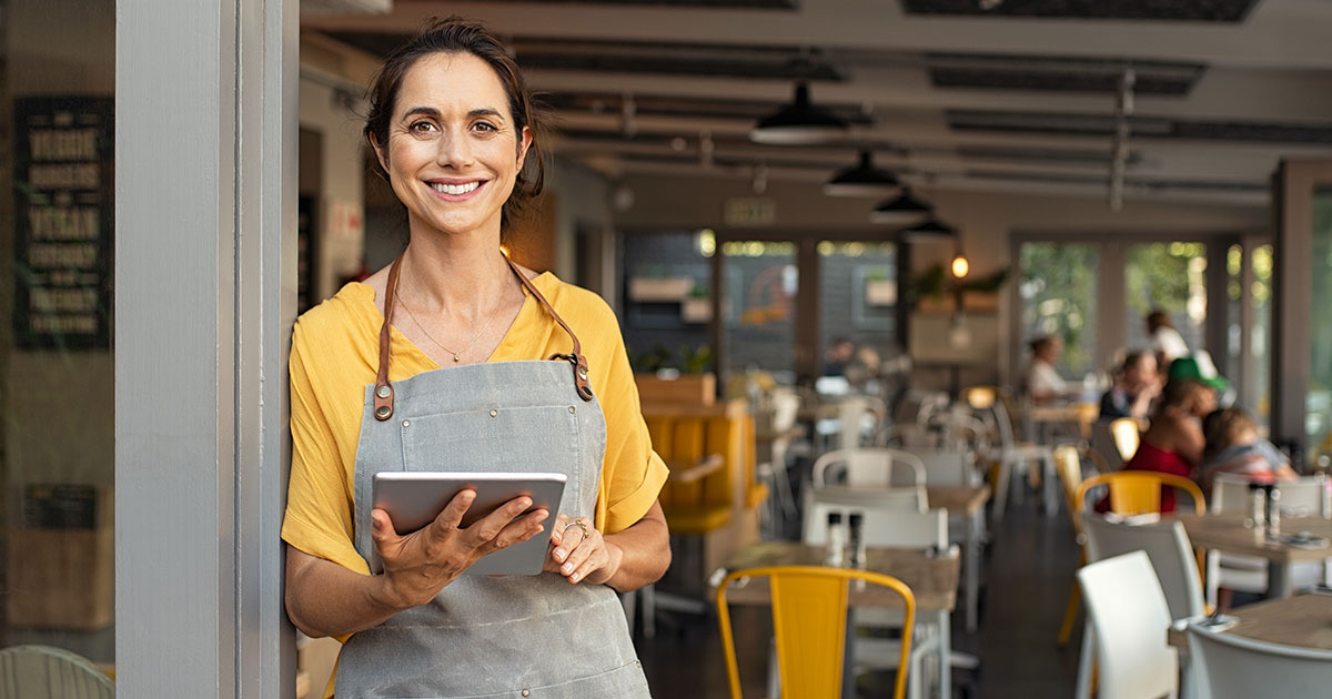 A local small business owner is standing in the doorway of her restaurant, thinking about local marketing.