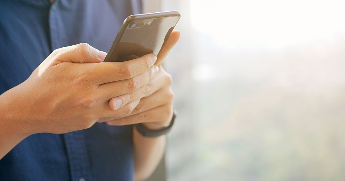 A person wearing a watch and a blue shirt holding their mobile phone with both hands.