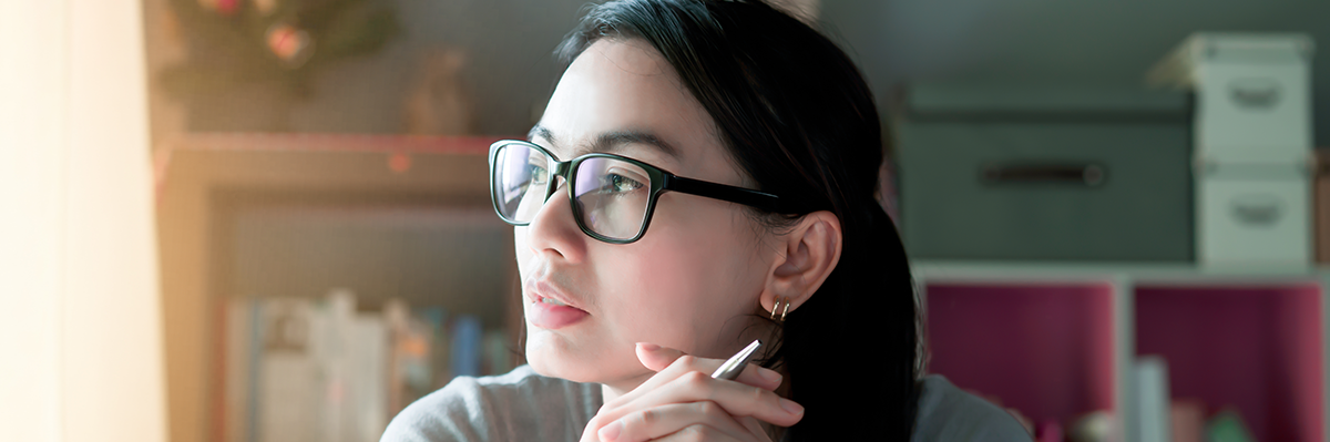 An Asian woman is holding a pen staring off in the distance, obviously thinking about something.