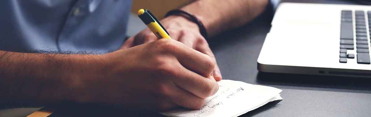 A man writing in a notebook with a pen.