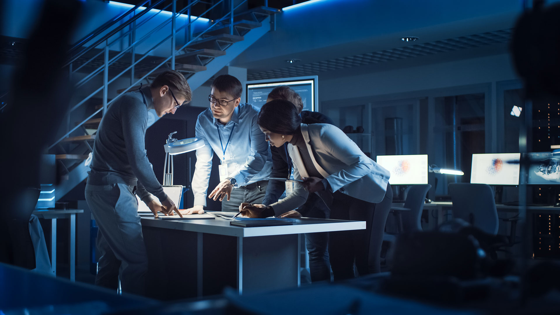 Group of business people standing over a table with a light shining on the table.