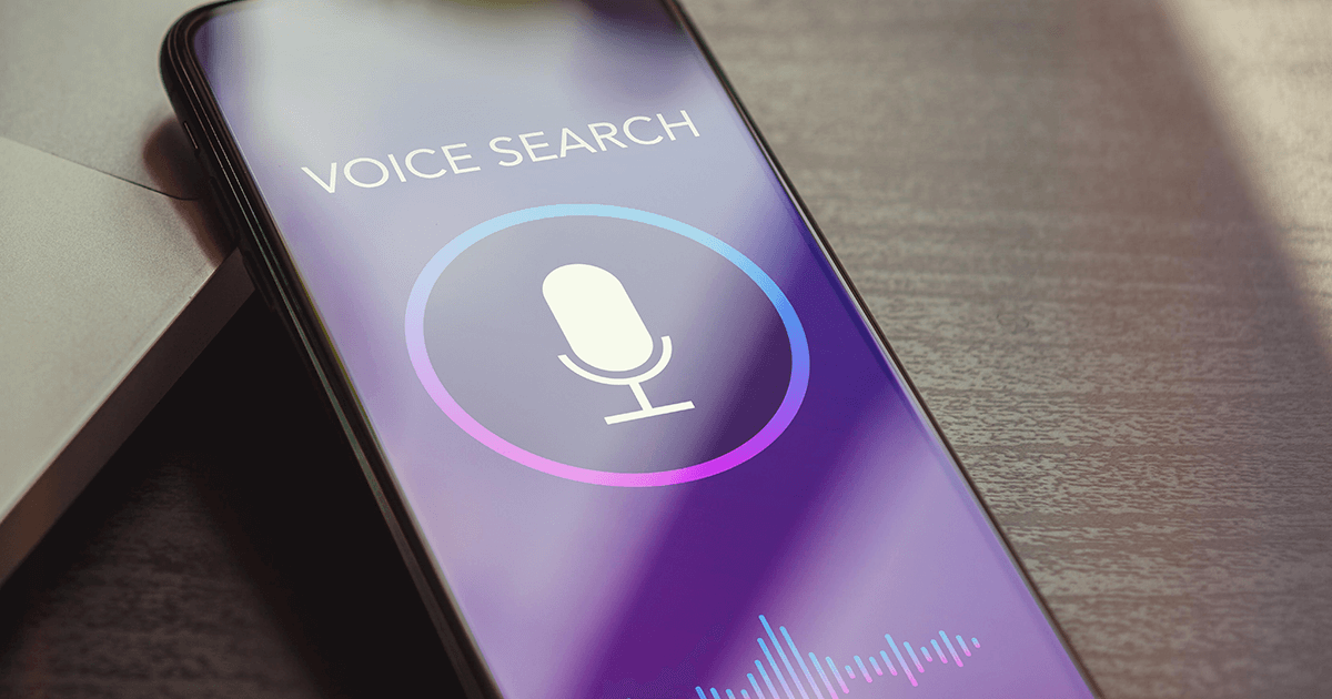 Cell phone sitting on desk with voice search on screen.